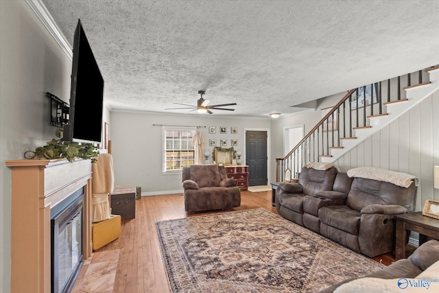 living area with stairway, a fireplace with flush hearth, a textured ceiling, light wood finished floors, and ceiling fan