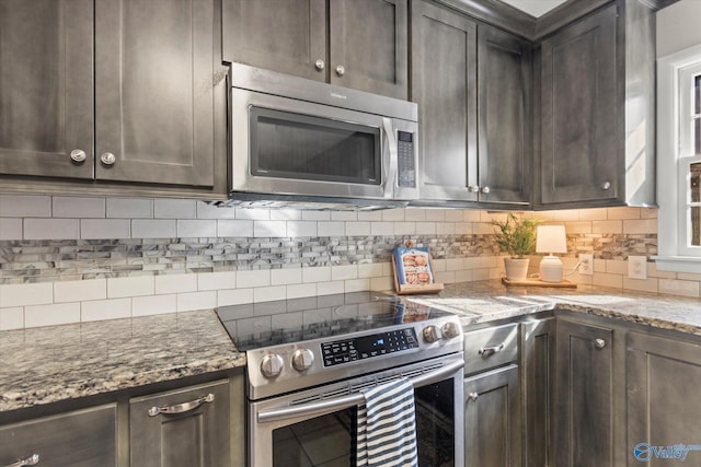 kitchen featuring dark brown cabinetry, decorative backsplash, light stone countertops, and appliances with stainless steel finishes