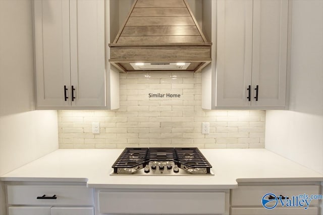 kitchen featuring white cabinetry, stainless steel gas cooktop, custom exhaust hood, and backsplash