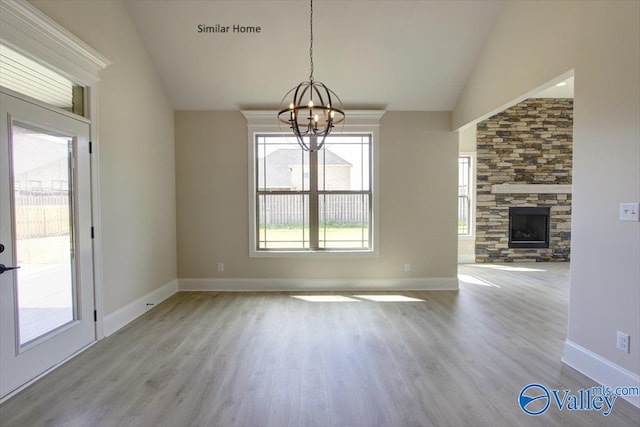 unfurnished dining area with a healthy amount of sunlight, a stone fireplace, a chandelier, and light hardwood / wood-style floors