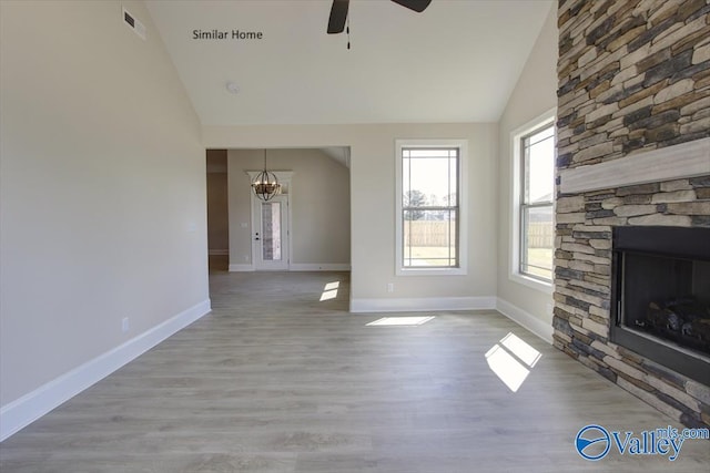 unfurnished living room featuring a stone fireplace, ceiling fan with notable chandelier, lofted ceiling, and light hardwood / wood-style floors