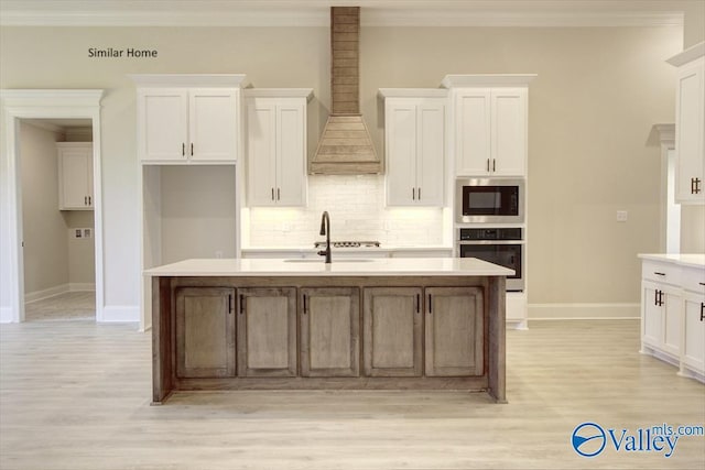 kitchen with a center island with sink, premium range hood, white cabinets, and appliances with stainless steel finishes