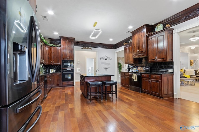 kitchen with dark countertops, black appliances, a kitchen breakfast bar, and dark wood-style flooring