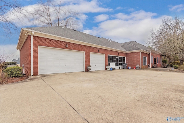 exterior space featuring a garage, driveway, brick siding, and a shingled roof