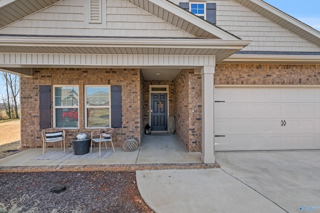 property entrance with brick siding, a porch, concrete driveway, and an attached garage