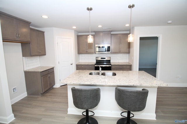 kitchen with light wood-type flooring, hanging light fixtures, appliances with stainless steel finishes, and an island with sink