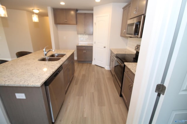 kitchen with appliances with stainless steel finishes, backsplash, sink, decorative light fixtures, and a center island with sink