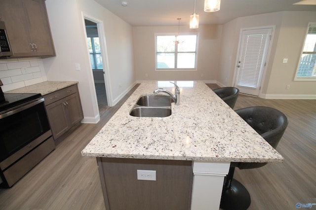 kitchen with a kitchen breakfast bar, sink, an island with sink, appliances with stainless steel finishes, and decorative light fixtures