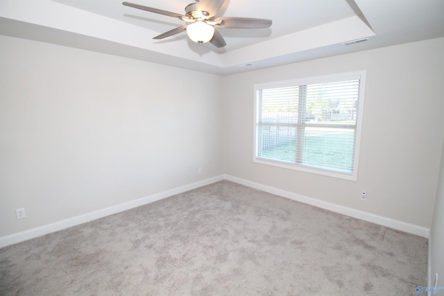 empty room with ceiling fan, a raised ceiling, and light colored carpet