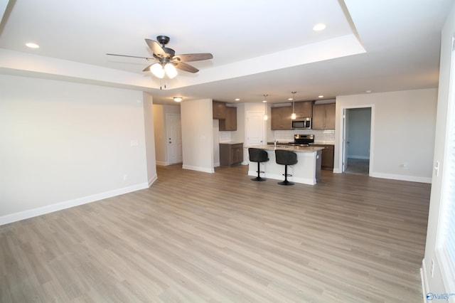 unfurnished living room featuring ceiling fan, a raised ceiling, and light hardwood / wood-style flooring