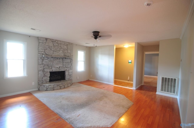 unfurnished living room featuring a stone fireplace, hardwood / wood-style floors, and ceiling fan