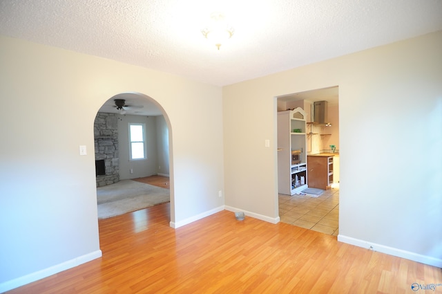 unfurnished room featuring a fireplace, light wood-type flooring, ceiling fan, and a textured ceiling