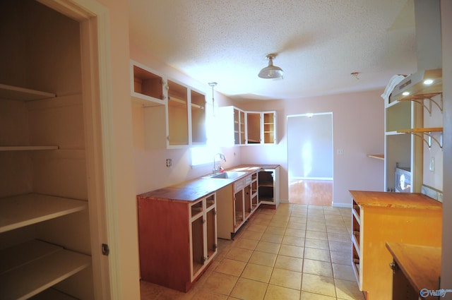 kitchen with light tile patterned floors, butcher block counters, a textured ceiling, hanging light fixtures, and sink