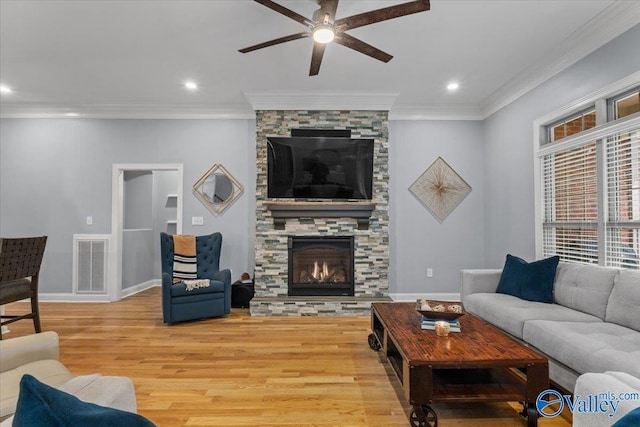 living room featuring light wood-type flooring, crown molding, a stone fireplace, and ceiling fan