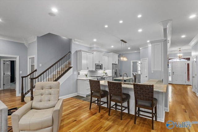 kitchen with stainless steel appliances, decorative light fixtures, light hardwood / wood-style floors, white cabinets, and a breakfast bar area