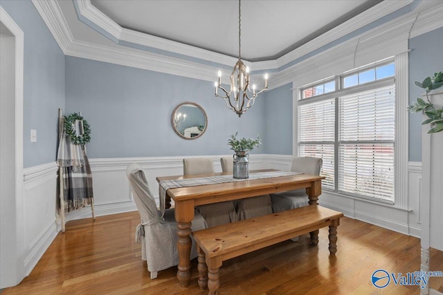 dining space with ornamental molding, a chandelier, light hardwood / wood-style floors, and a raised ceiling