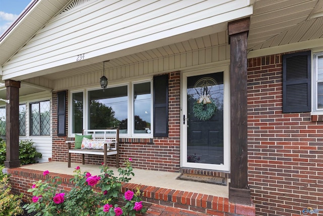 doorway to property with a porch and brick siding