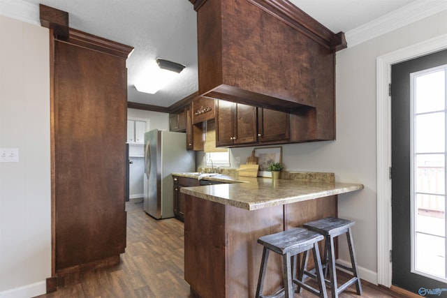 kitchen with a breakfast bar area, crown molding, freestanding refrigerator, baseboards, and dark wood-type flooring