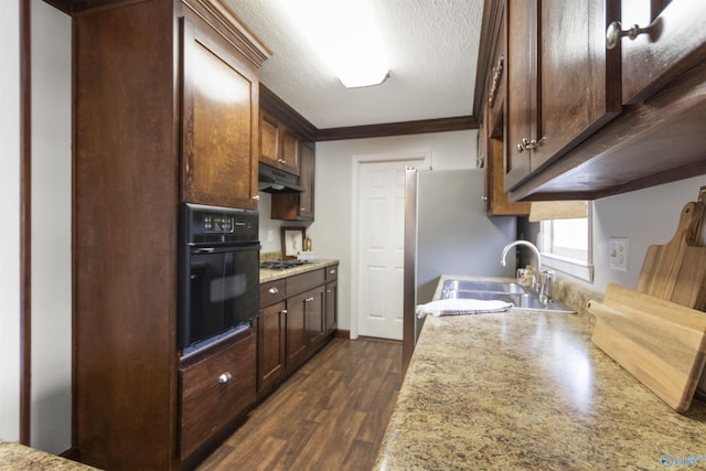 kitchen featuring under cabinet range hood, light countertops, black oven, a sink, and crown molding