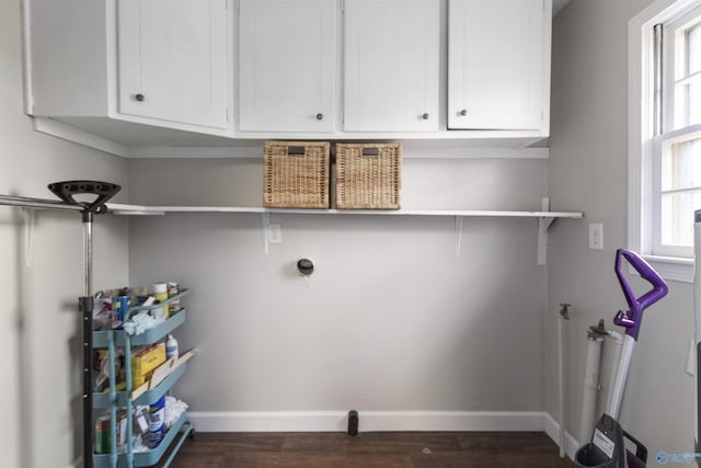 laundry area with dark wood finished floors, baseboards, a wealth of natural light, and cabinet space