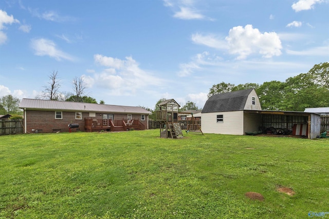 view of yard featuring a deck, fence, an outbuilding, and a playground