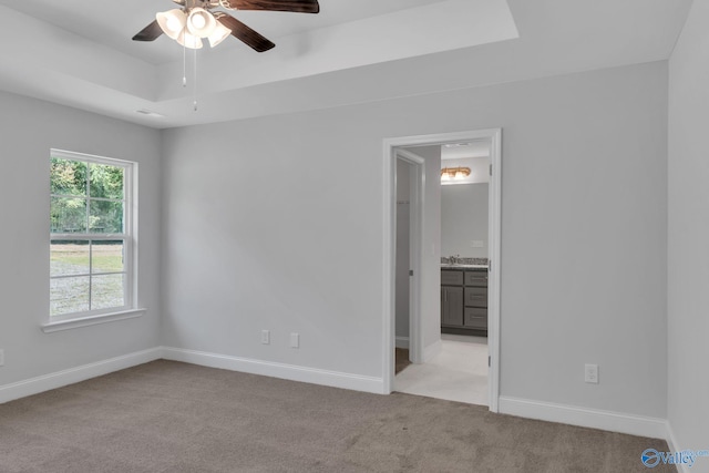 unfurnished bedroom featuring baseboards, a tray ceiling, ensuite bathroom, and light colored carpet