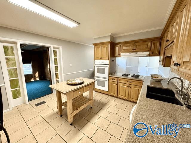 kitchen with sink, white appliances, ornamental molding, and light tile patterned floors