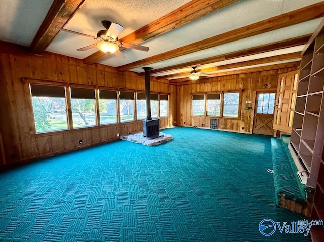 interior space featuring beamed ceiling, a wood stove, ceiling fan, and wood walls