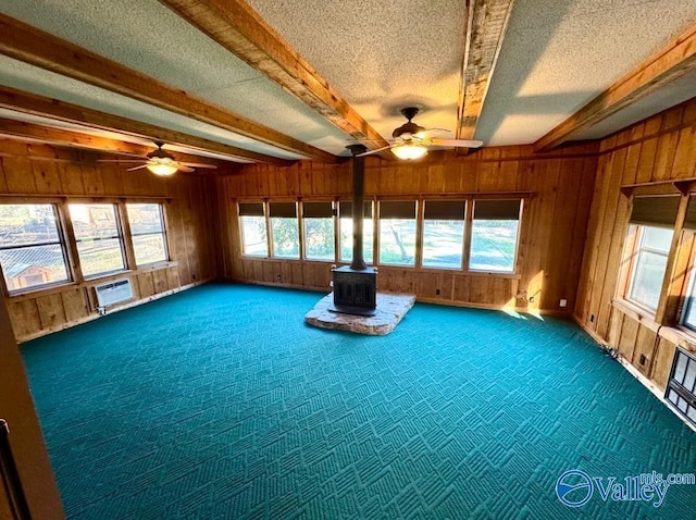 unfurnished sunroom with beamed ceiling, ceiling fan, a healthy amount of sunlight, and a wood stove