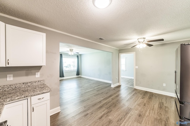 unfurnished living room featuring light wood-type flooring, a textured ceiling, a ceiling fan, and visible vents
