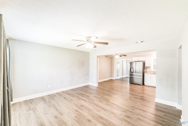unfurnished living room with light wood-style floors, visible vents, ceiling fan, and a textured ceiling