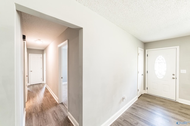 foyer entrance featuring a textured ceiling, baseboards, and wood finished floors