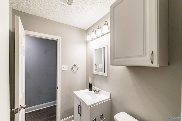half bathroom with a textured ceiling, toilet, visible vents, vanity, and wood finished floors