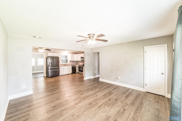 unfurnished living room with a sink, visible vents, ceiling fan, light wood-style flooring, and baseboards