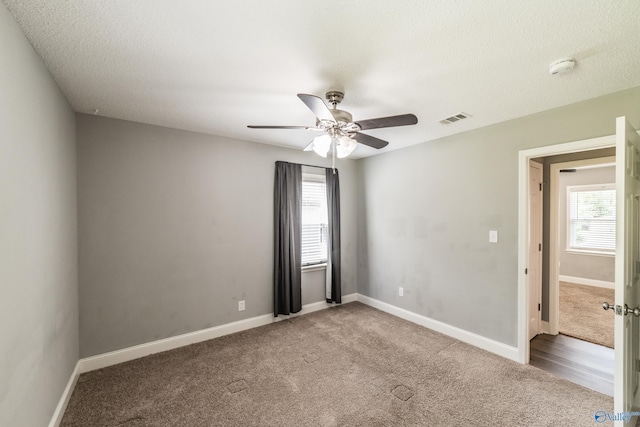unfurnished room with carpet, a wealth of natural light, visible vents, and ceiling fan