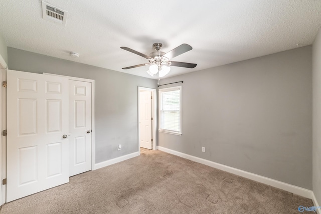 unfurnished bedroom with a textured ceiling, visible vents, carpet floors, a ceiling fan, and baseboards