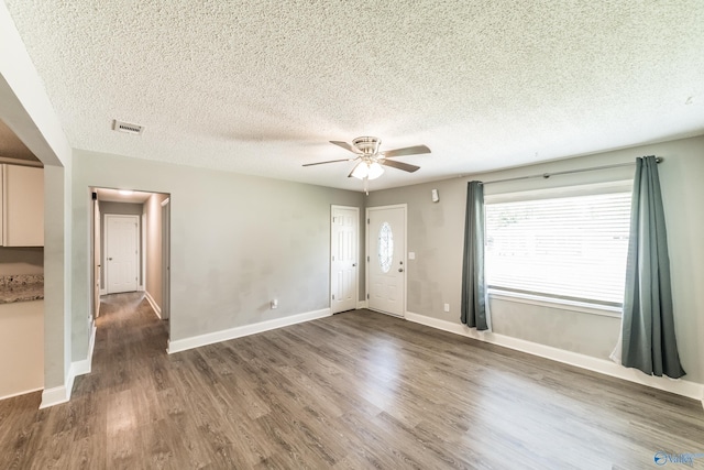 interior space featuring a ceiling fan, a textured ceiling, baseboards, visible vents, and wood finished floors