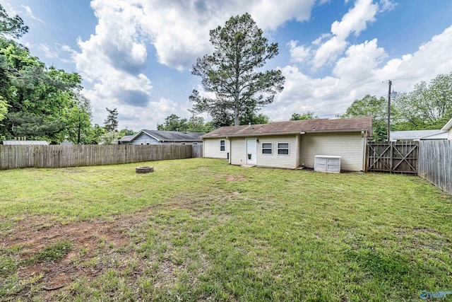 back of house featuring an outdoor fire pit, a lawn, and a fenced backyard