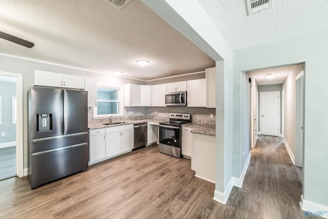 kitchen with light wood finished floors, a textured ceiling, stainless steel appliances, and a sink