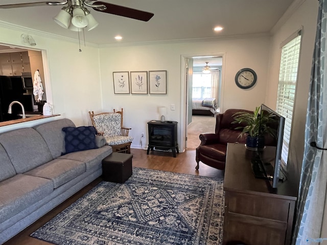 living area featuring wood finished floors, a wood stove, ornamental molding, and ceiling fan