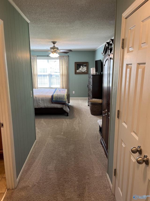 bedroom featuring a textured ceiling, a ceiling fan, carpet floors, wooden walls, and baseboards