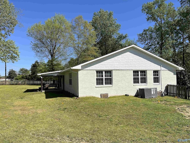 back of property with central AC, brick siding, fence, and a lawn