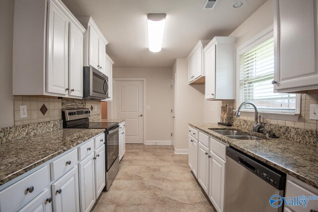 kitchen featuring tasteful backsplash, dark stone counters, stainless steel appliances, sink, and white cabinetry