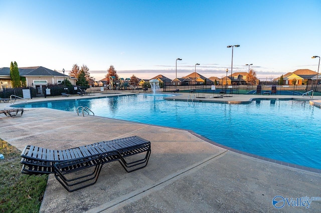 pool at dusk with pool water feature and a patio area