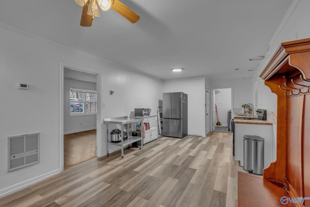 kitchen featuring heating unit, ceiling fan, crown molding, light hardwood / wood-style floors, and stainless steel refrigerator