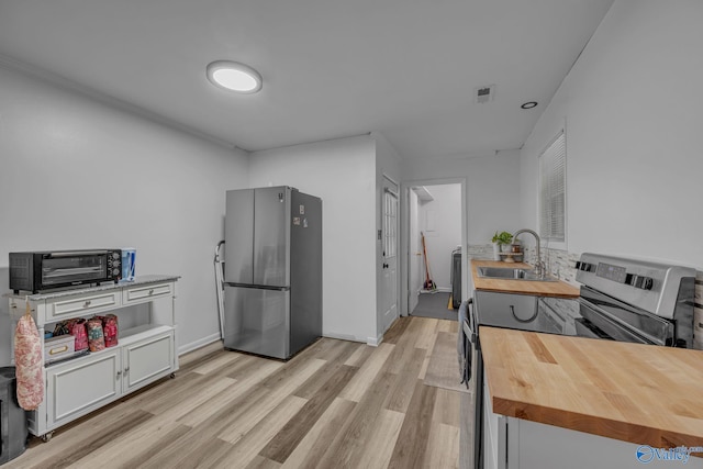 kitchen with wooden counters, light wood-type flooring, stainless steel appliances, sink, and white cabinets