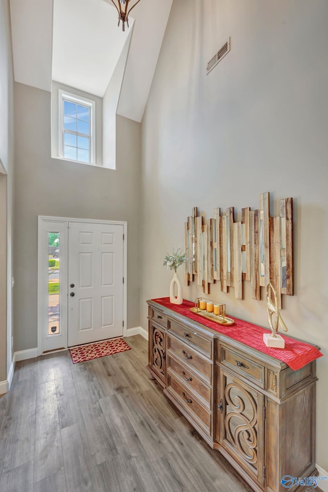 foyer with wood finished floors, high vaulted ceiling, plenty of natural light, and visible vents