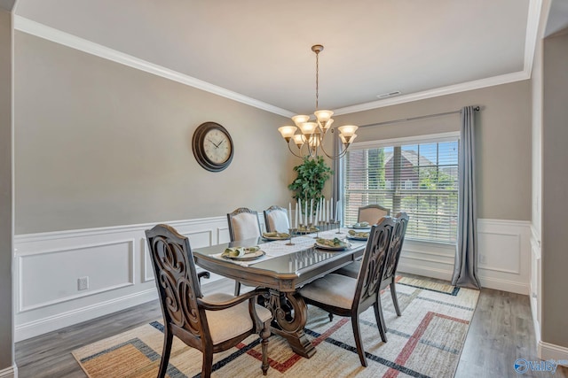 dining space with a wainscoted wall, light wood-type flooring, a chandelier, and ornamental molding
