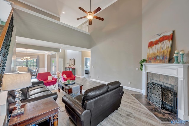 living room with ceiling fan with notable chandelier, wood finished floors, crown molding, baseboards, and a tiled fireplace