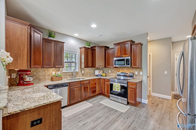 kitchen featuring a sink, tasteful backsplash, light wood-type flooring, light stone countertops, and appliances with stainless steel finishes